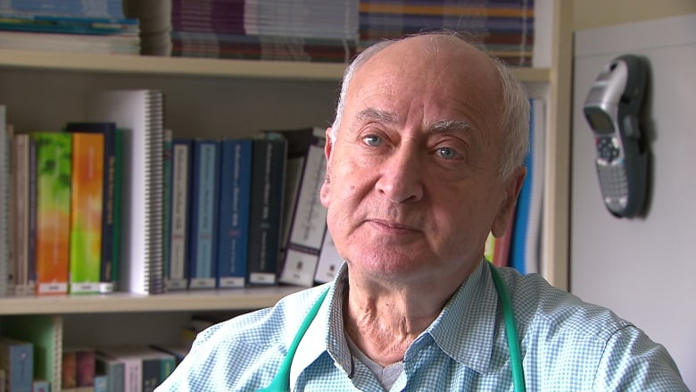 A man in a collared shirt with a stethoscope around his neck is pictured in front of a book case