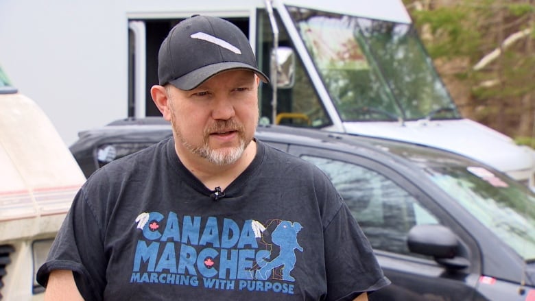 A man looks at the camera in front of a camper. 