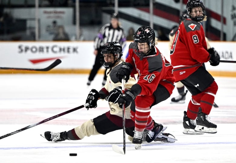 A hockey player stickhandles the puck away from a falling opponent during a game.