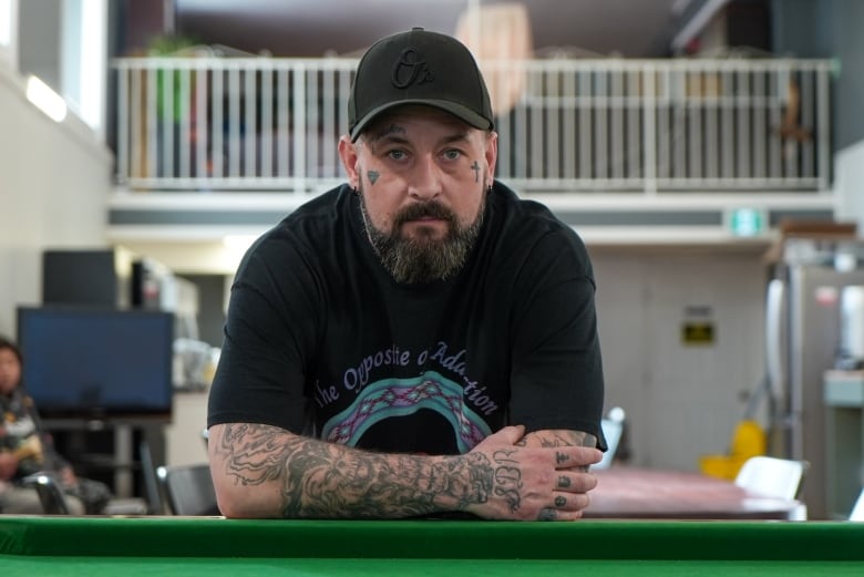 A person wearing a black baseball gap leans over a green pool table.