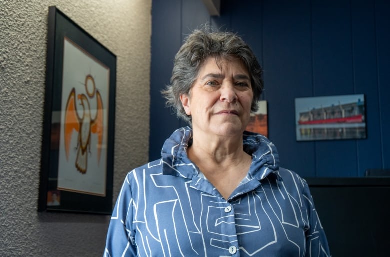 A person wearing a periwinkle-blue shirt with white stripes stands in a room, looking forward.