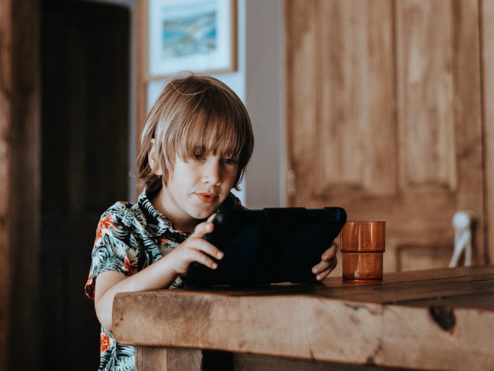 Little boy playing Roblox on tablet in kitchen.