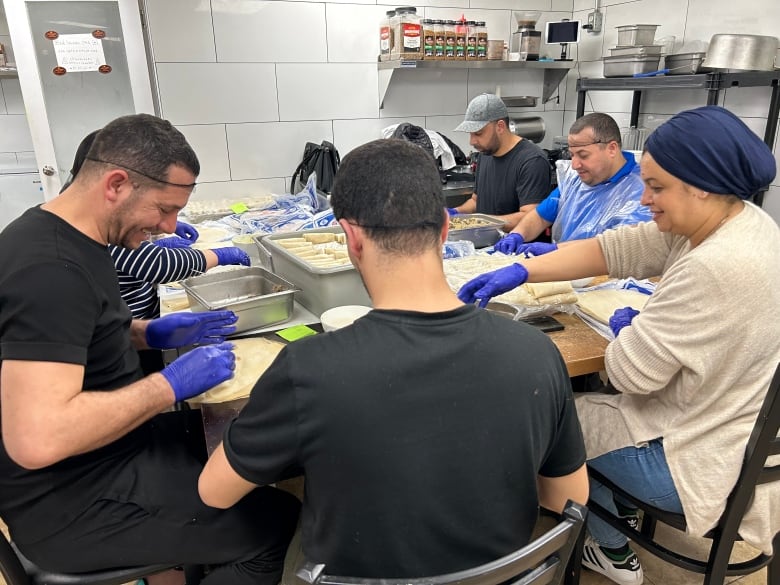 Men and women wearing blue kitchen gloves and hair nets smile as they work together around a table.