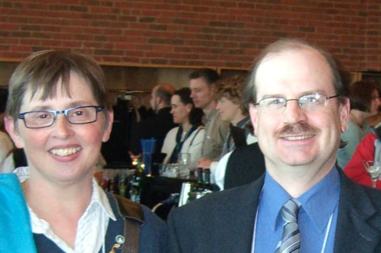 A man and a woman in formal wear smile at the camera.