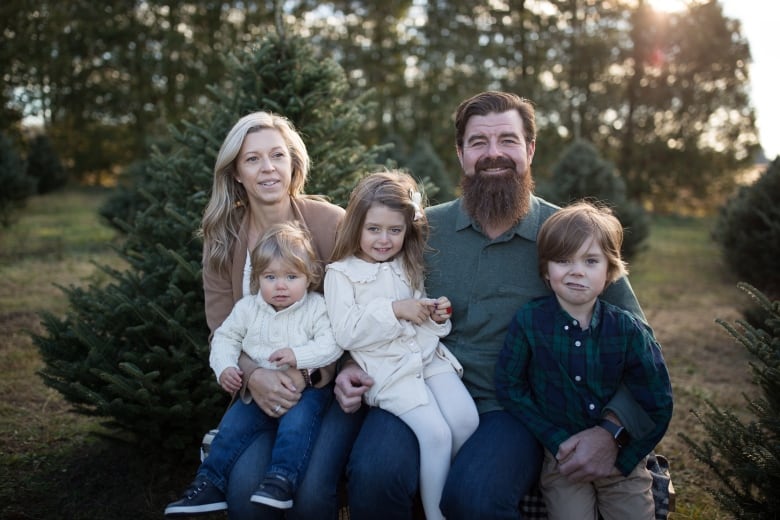 A mother and father sit outside with their three young children on their laps.