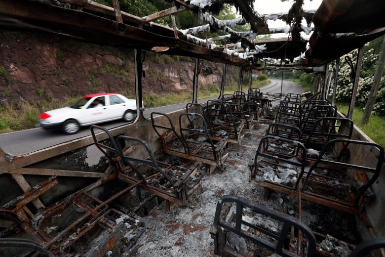 The burnt-out remains of a bus are seen along a forested road. 