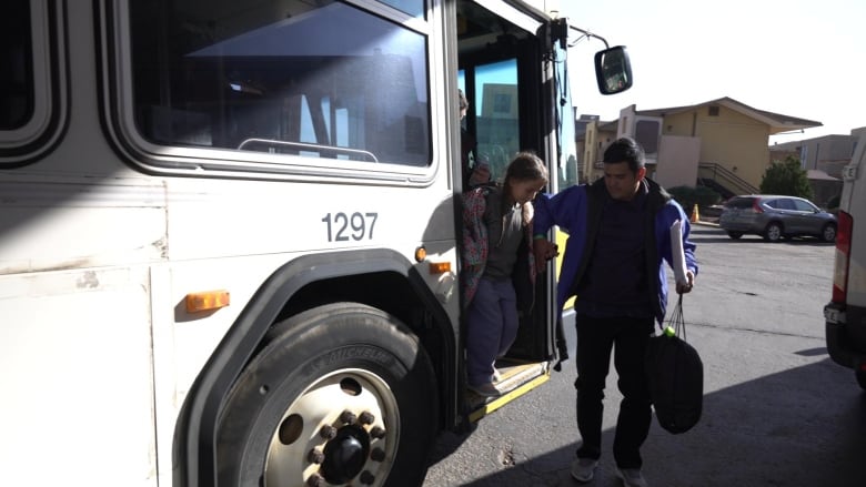 A man holds a girl's hand to help her get off the bus. 