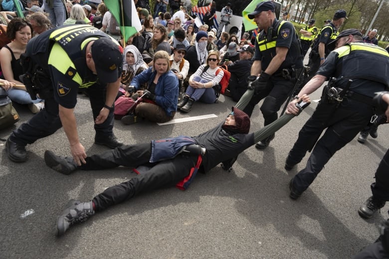 A protesters is dragged away by police officers as others sitting on the ground look on.