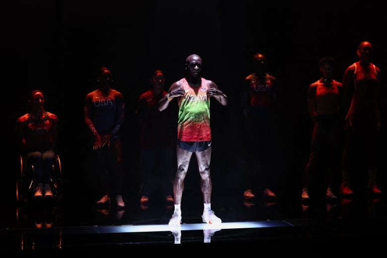 A man  stands on a stage wearing  shorts and a t-shirt