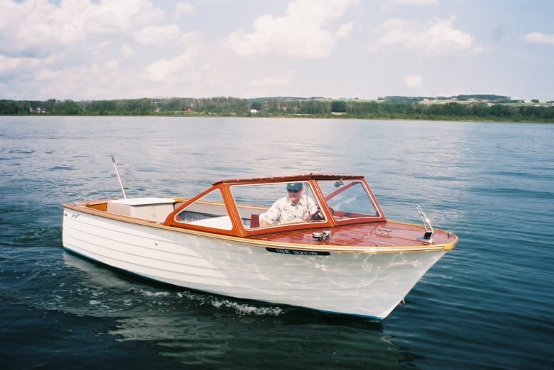 A man wearing glasses inside a simple boat on a lake. 