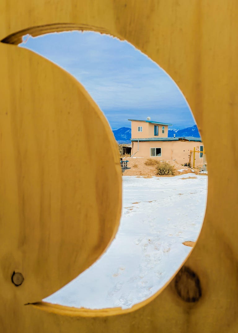 Looking through a crescent moon cutout toward an off-grid house.