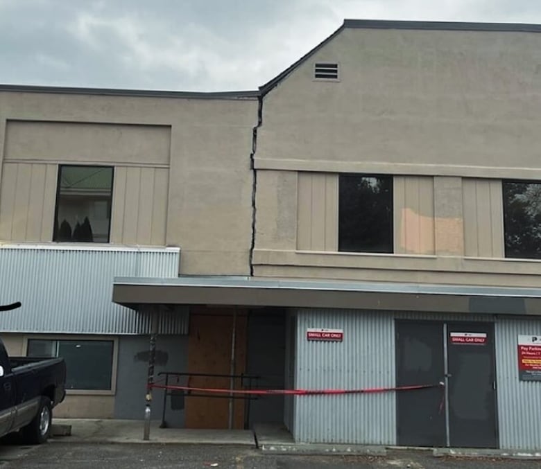 A large grey and beige building has a crack in the upper level wall. 