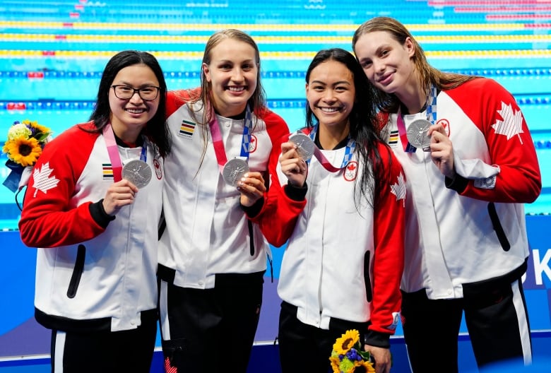 Four swimmer smiles while holding silver medals.