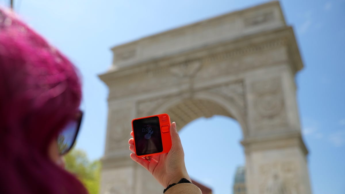 A woman holding up the Rabbit R1 in front of Washington Square Park