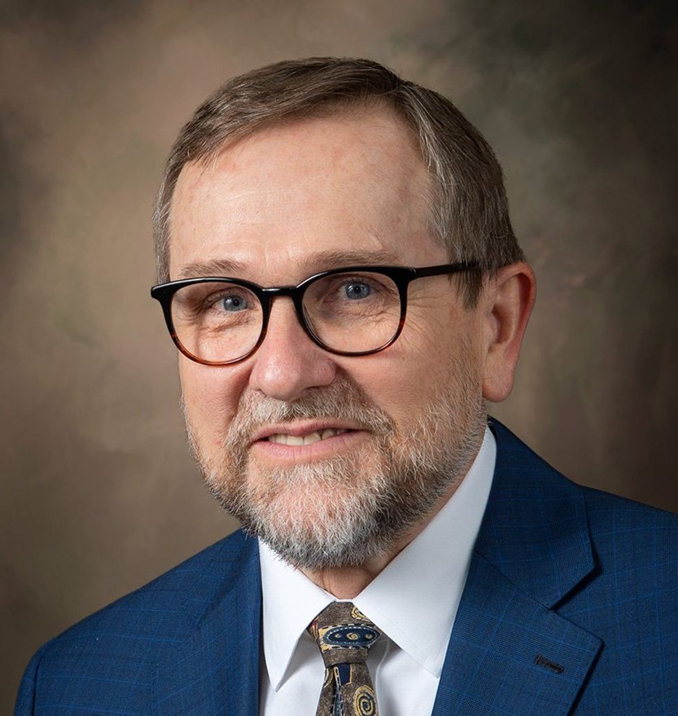 Photo of a smiling, bearded man in a blue jacket.  