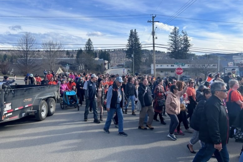 A large crowd of people walks down a city street on their way to Quesnel city hall. 