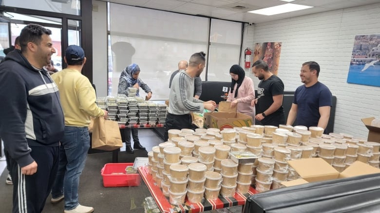 Smiling people are working near tables filled with individually packaged foods.