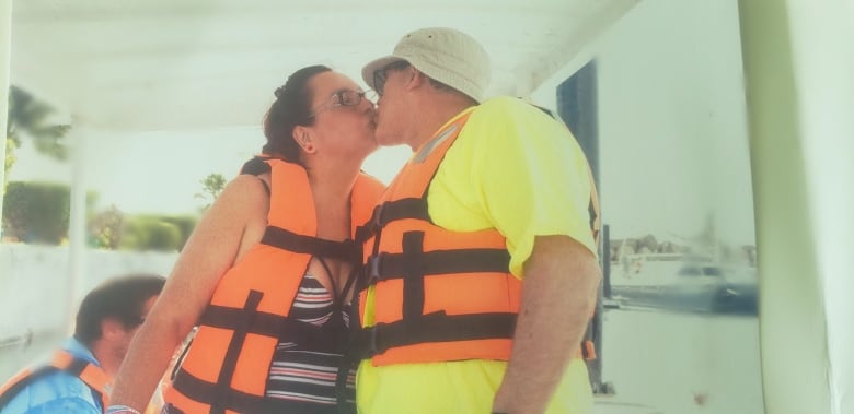 A man and woman kiss. They are both wearing bright swimwear and life jackets. 