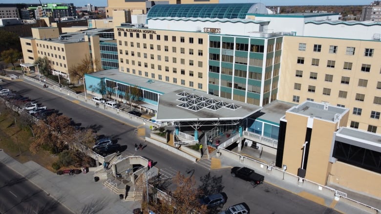 An aerial view of a large, tan building with many windows. It says "Royal Alexandra Hospital" near the top. There are cars parked outside.