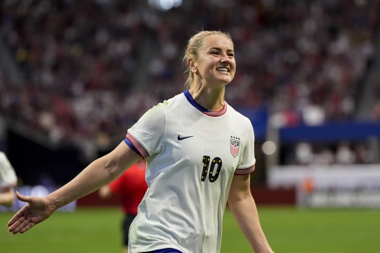 A women's soccer player extends her arms in celebration.