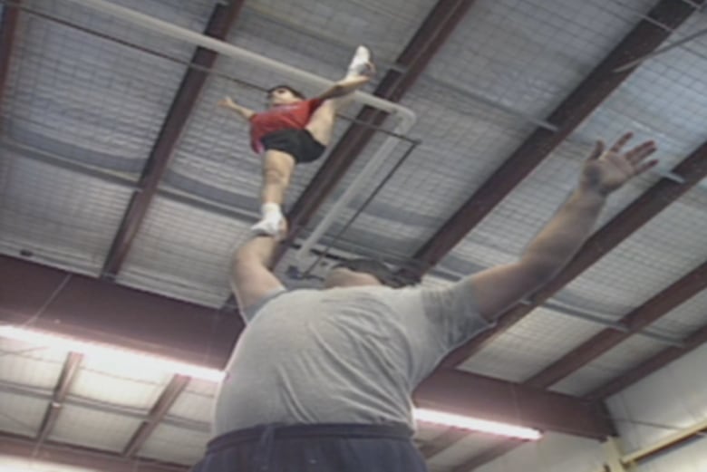 A large man balances a small boy on one hand , held high above his head.