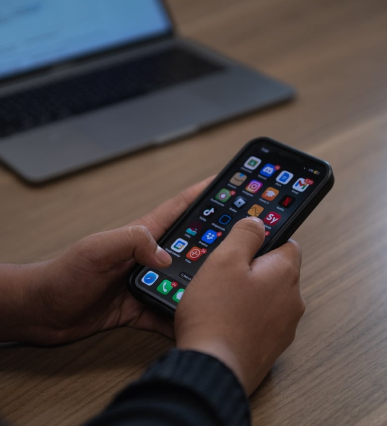 A close-up image of a teen boy holding a smartphone, his thumbs hovering over the apps -- including TikTok and Instagram -- on his home screen.