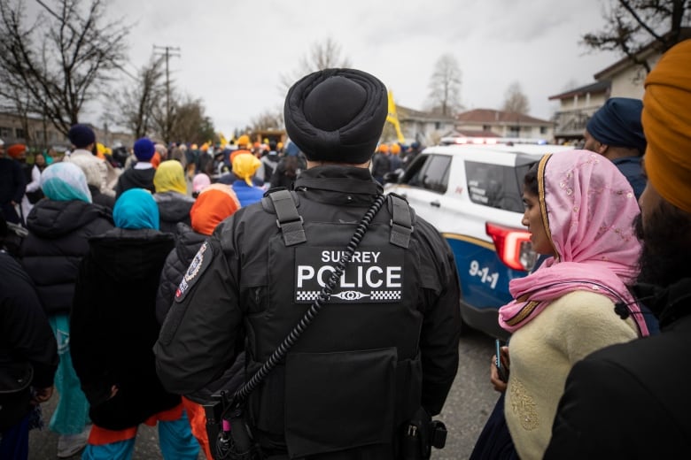 A police officer with the words 'Surrey Police' stands behind a procession of people.