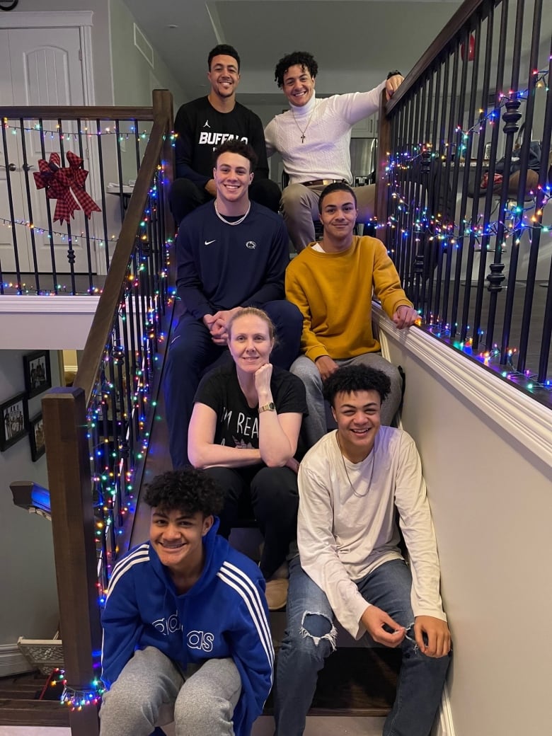 Six boys sit with a woman, their mom, on the stairs with Christmas lights