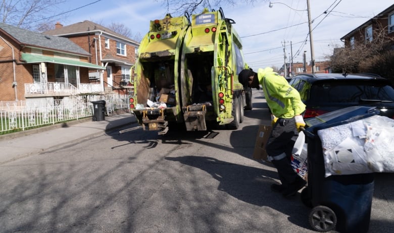 A worker pulls a full recycling bin toward a truck. 