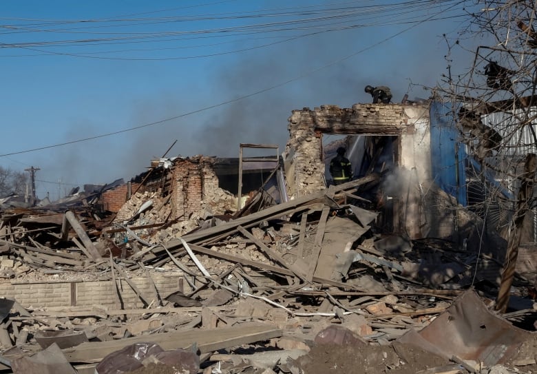 Several one-story buildings are shown destroyed, with smoke rising and wooden and concrete debris littering the ground.