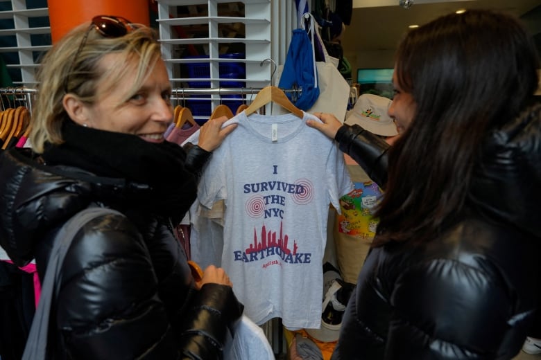 People hold up a shirt that reads, 'I survive the NYC earthquake,' inside a store.