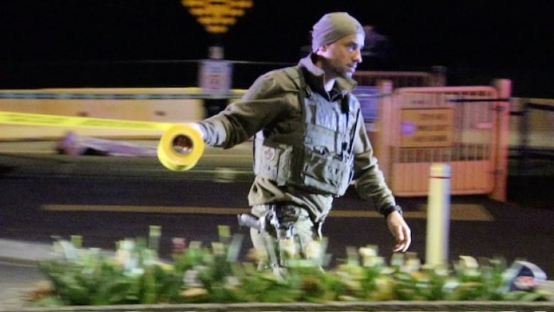 A man in tactical uniform holds a roll of yellow tape. The image is slightly blurred to convey movement.