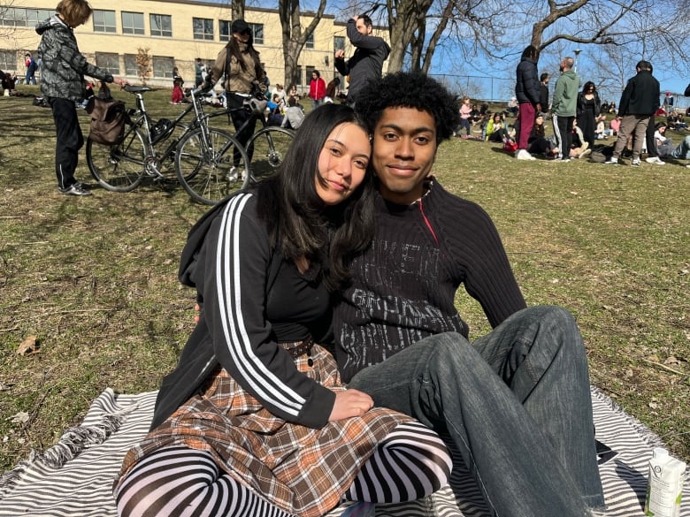 A young couple sit on a blanket on some grass in a parc