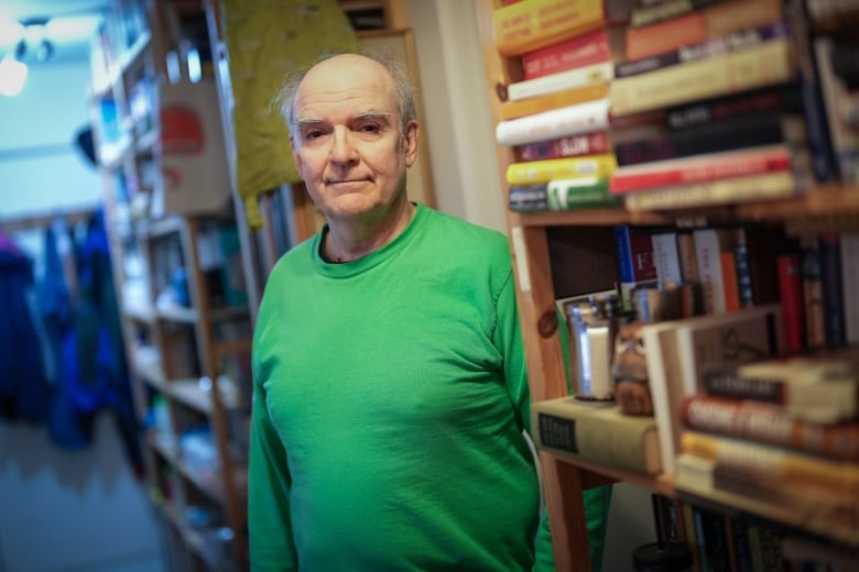 A man stands next to a book shelf.