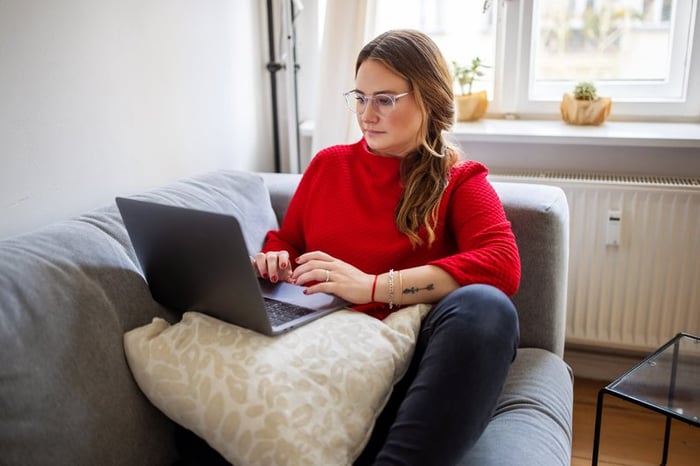 A person typing on a laptop while sitting comfortably on a couch.