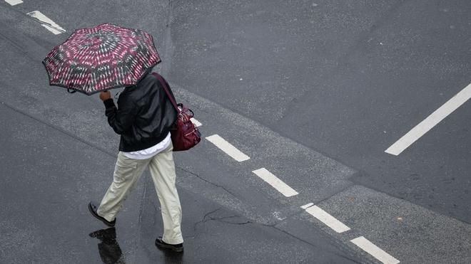 Wetter: Eine Passantin geht bei Regen über die Straße.