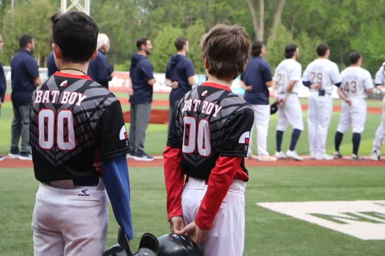 A couple of kids wearing jerseys with "bat boy" on the back, line up on the field. 