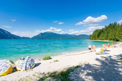 Am Strand am tiefblauen Walchensee genießen Urlaubende den Sonnenschein.