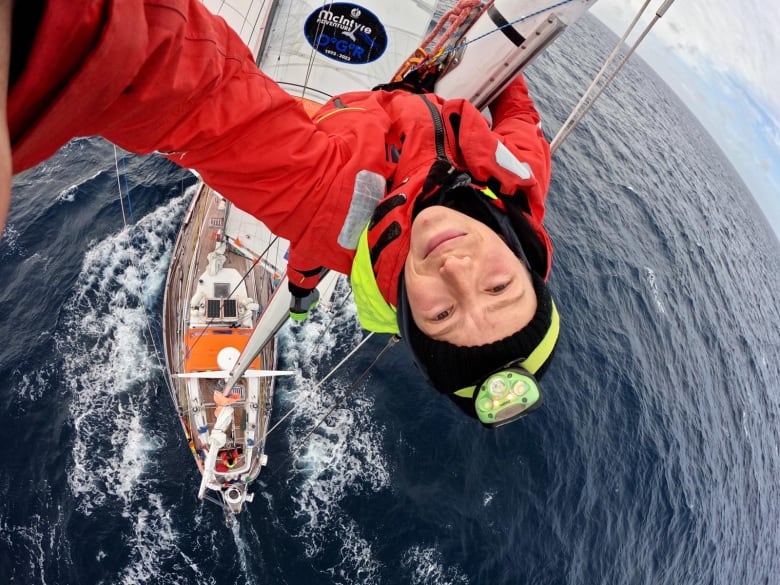 A woman takes a selfie as she is up on the mast of a sailboat 