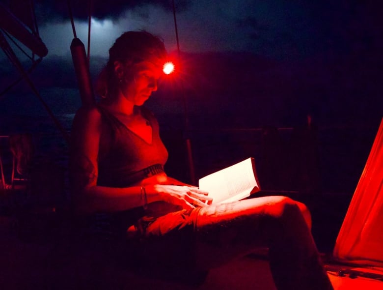 A woman reads a book using a headlight