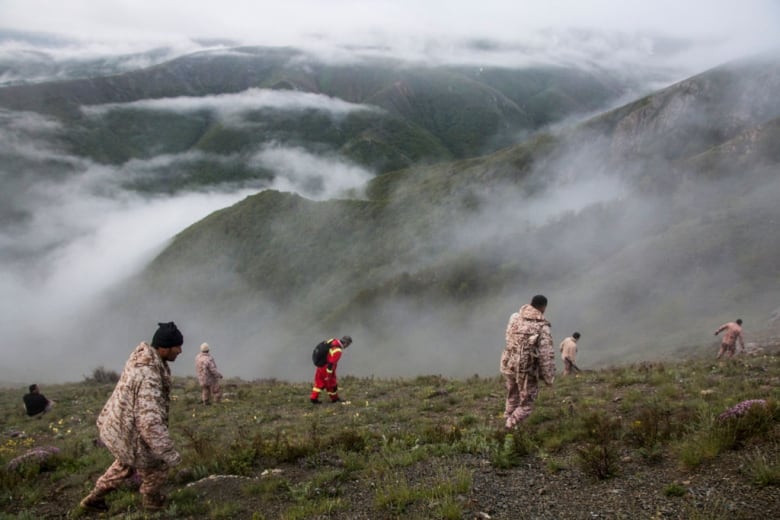 Rescuers walk in a mountainous region to look for helicopter wreckage. 