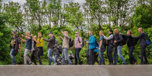 Männer gehen hintereinander in einem Wald und halten sich and Schultern