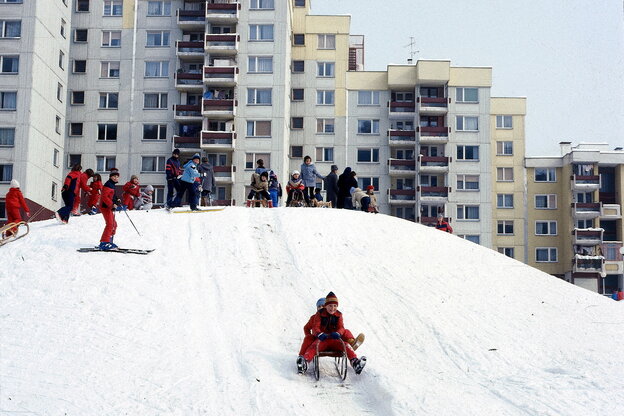 Kinder fahren Schlitten auf einem schneebedeckten Hügel vor einer Häuserlandschaft