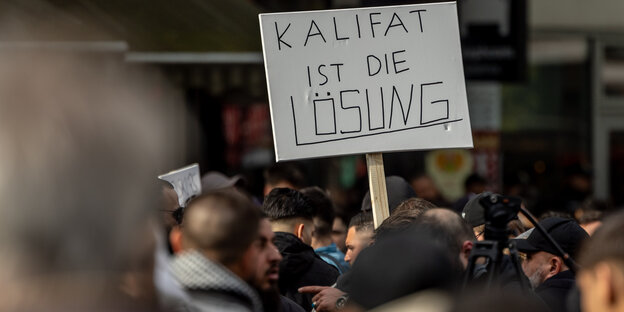 Mehrere Demonstranten stehen beieinander, einer hält ein Schild hoch, auf dem steht 