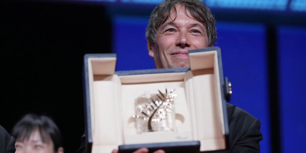 Preisträger Sean Baker beugt sich über die Trophäe von Cannes