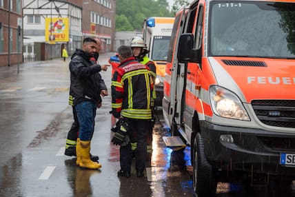 Saarland, Saarbrücken: Anwohner Osman Bilgic (l.) spricht mit Feuerwehrleuten über die Lage in der überschwemmten Fischbachstraße. In seinem Haus ist der Keller überflutet. 