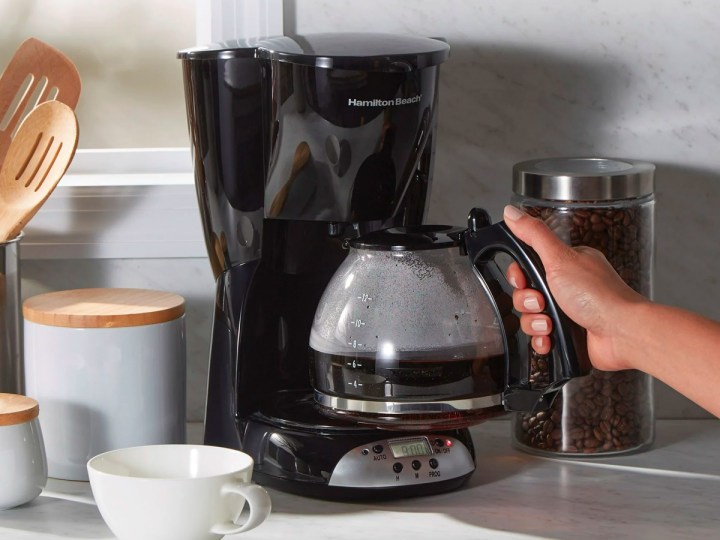 A hand removes the carafe from the Hamilton Beach 12-cup coffee maker.