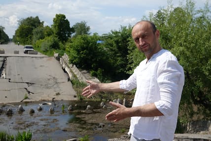 Ukraine, Tschernihiw: Viktor Jerko zeigt die Zerstörungen an der Brücke über den Fluss Stryschen. Die Straßenbrücke wurde im Februar 2022 von ukrainischen Truppen gesprengt, um den russischen Vormarsch zu stoppen. 