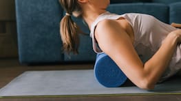 Caucasian brunette lying on a foam roller on a mat in her living room, stretching her back after a workout.