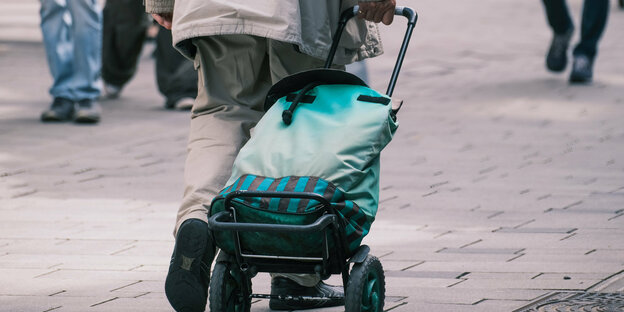 Eine ältere Person zieht einen Trolley durch eine Fußgängerzone